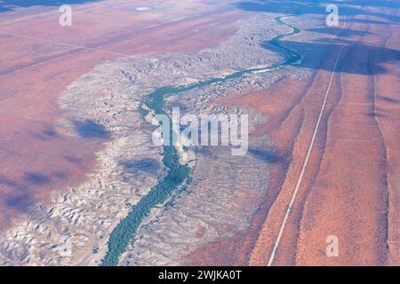 Luftlandschaft mit abgenutzten Ufern des Flusses Nossob und Schotterstraße an roten Sanddünen in der Kalahari-Wüste, aufgenommen von einem Segelflugzeug im hellen späten Frühling Stockfoto