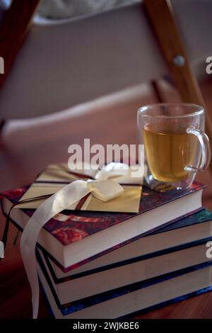 Ein Geschenkgutschein neben dem perfekten Ort zum Lesen und Entspannen, ein weißer Sessel umgeben von Büchern in einem hellen Raum Stockfoto