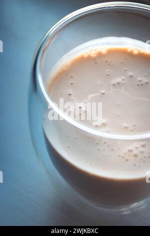 Cremiger Kaffee auf beigefarbenem Hintergrund mit Kopierraum. Milchschaum mit Espresso im Glas. Frappe im Glas auf dem Tisch in pfirsichfarbener Fuzz-Farbe. Kalter Cappuccino. Stockfoto