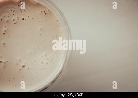 Cremiger Kaffee auf beigefarbenem Hintergrund mit Kopierraum. Milchschaum mit Espresso im Glas. Frappe im Glas auf dem Tisch in pfirsichfarbener Fuzz-Farbe. Kalter Cappuccino. Stockfoto