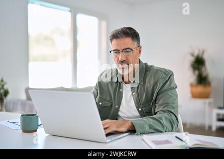 Ernster älterer Mann mit Brille am Laptop-Computer am Heim-Tisch. Stockfoto
