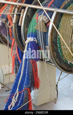 Zusammengerollte, bunte industrielle Fischernetze auf einer Winde an Bord eines Fischerbootes oder Trawlers Stockfoto