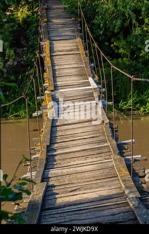 Alte Hängebrücke über den Fluss auf dem Land, die in die Perspektive geht. Stockfoto