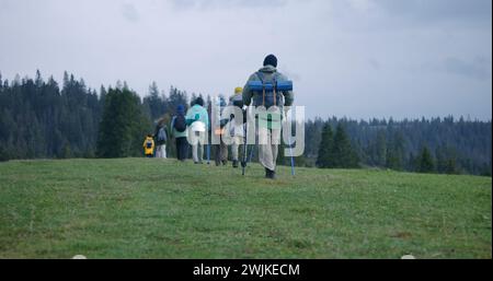 Eine Gruppe von Touristen mit Rucksäcken und Trekkingstöcken spaziert entlang des Wanderwegs auf dem wunderschönen Berg. Wanderer entdecken atemberaubende Naturlandschaften. Tourismus und aktives Freizeitkonzept. Zeitlupe. Rückansicht. Stockfoto