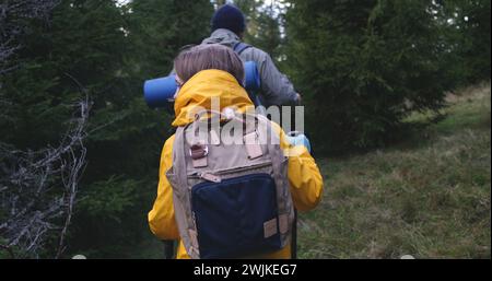 Kaukasisches Paar steht zwischen den Bäumen im Wald, schaut in die Kamera. Touristenfamilie während der Wanderung oder Wanderung in den Bergen im Urlaub. Gruppe von multiethnischen Wanderern, die im Hintergrund laufen. Outdoor-Enthusiasten. Stockfoto