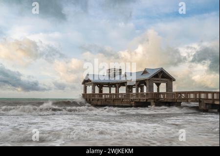 Ein hölzerner Pier, mit einem überdachten Teil am Ende, der in ein abgehacktes, raues Meer reicht Stockfoto