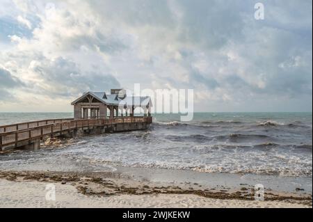 Ein hölzerner Pier, mit einem überdachten Teil am Ende, der in ein abgehacktes, raues Meer reicht Stockfoto