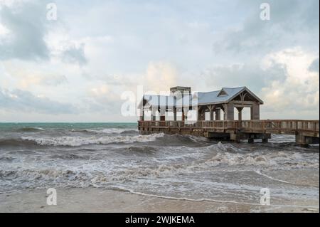 Ein hölzerner Pier, mit einem überdachten Teil am Ende, der in ein abgehacktes, raues Meer reicht Stockfoto