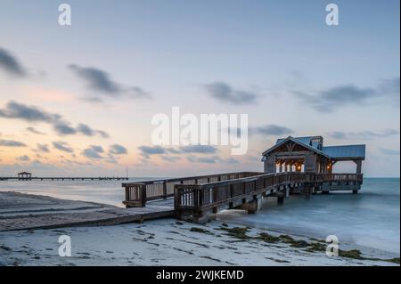 Holzpier in Key West, Florida, der bei Sonnenaufgang in das ruhige tropische Wasser des Ozeans reicht. Es gibt einen Hauch von Orange am Himmel Stockfoto