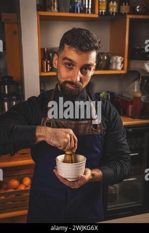 Der Barkeeper mischt Matcha-Grüntee-Pulver mit heißem Wasser in einer weißen Schüssel mit einem Bambus-Matcha-Schneebesen Stockfoto