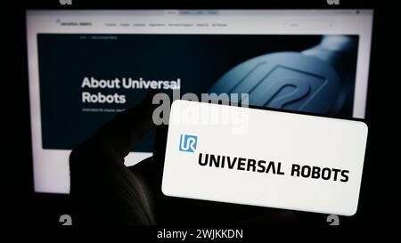 Person mit Smartphone mit Logo des dänischen Cobot-Unternehmens Universal Robots WIE vor der Website. Schwerpunkt auf dem Display des Telefons. Stockfoto