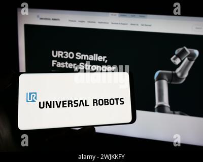 Person, die ein Handy mit dem Logo des dänischen Cobot-Unternehmens Universal Robots hält, WIE vor der Webseite. Schwerpunkt auf dem Display des Telefons. Stockfoto