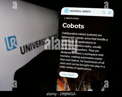 Person, die ein Mobiltelefon mit der Website des dänischen Cobot-Unternehmens Universal Robots vor dem Logo hält. Konzentrieren Sie sich auf die Mitte des Telefondisplays. Stockfoto