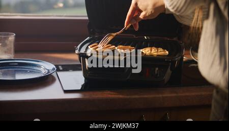 Nahaufnahme einer Frau, die die Schüssel in den Händen hält und den Teig mit einem Löffel auf den Grill legt. Zwei Frauen kochen zusammen Pfannkuchen zum Frühstück. Die Familie von Touristen hielt während der Urlaubsreise im Ferienhaus an. Stockfoto