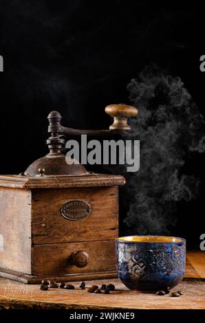 Alte Kaffeemühle mit orientalischer Keramik-Kaffeetasse, auf Holzoberfläche und dunklem Hintergrund Stockfoto
