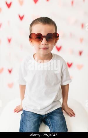 Glücklicher Junge mit herzförmiger Sonnenbrille auf Herzgirlande Hintergrund Stockfoto