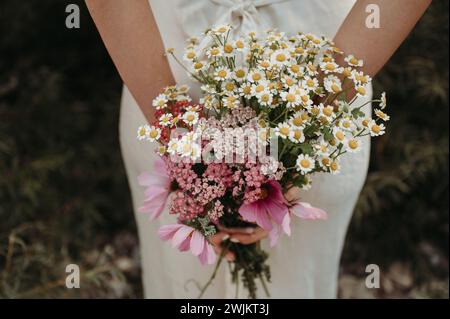 Frau in einem weißen Kleid, die einen Haufen wilder Blumen in den Händen hält Stockfoto