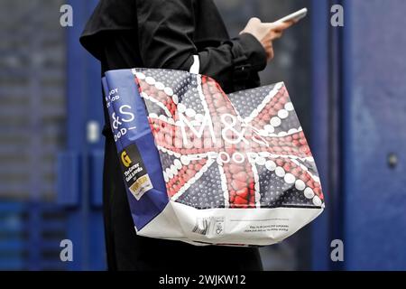 Eine Frau mit Marks and Spencer Tasche, die ein Handy benutzt Stockfoto