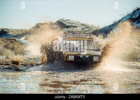 Ein hintergrundbeleuchteter SUV fährt durch eine Pfütze in den Bergen. Stockfoto