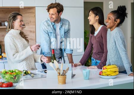 Eine Gruppe von Freunden trinkt Wein, während sie an der Küche hängen Stockfoto