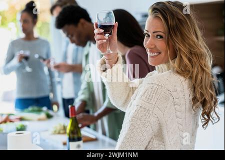 Fröhliche Erwachsene Frau, die auf die Kamera zurückblickt, während sie Weingläser hochhebt Stockfoto