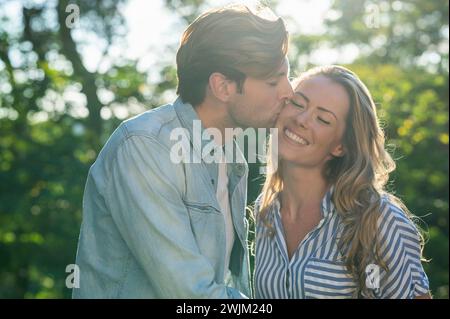Erwachsener Mann, der Freundin auf die Wange küsst, während er draußen steht Stockfoto