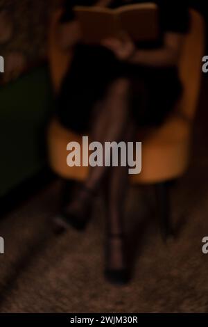 Verschwommenes Foto von der unteren Hälfte der Frau, die in einem dunklen Zimmer auf einem Stuhl sitzt Stockfoto