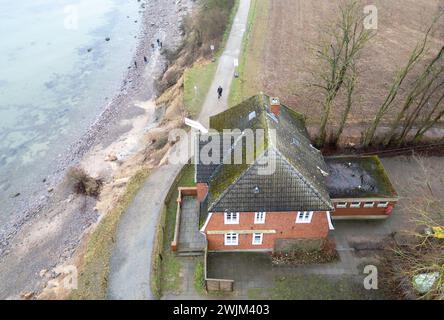 PRODUKTION - 14. Februar 2024, Schleswig-Holstein, Lübeck-Travemünde: Blick auf die Klippen und das Jugendzentrum Haus Seeblick der Jugendorganisation SJD - die Falken, auf die Klippen in Brodten an der Ostsee (Drohnenaufnahme). Das Jugendzentrum Haus Seeblick, direkt an den Brodtenfelsen gelegen, ist nach einem weiteren Randabbruch für Kinder- und Jugendarbeit geschlossen. Nur gut vier Meter liegen zwischen einer Ecke des 'Haus Seeblick' und dem Abgrund. Ende Januar fiel ein Baum entlang des Randes und hinterließ ein Loch im Fußweg vor dem Haus. Foto: Marcus Brandt/dpa Stockfoto