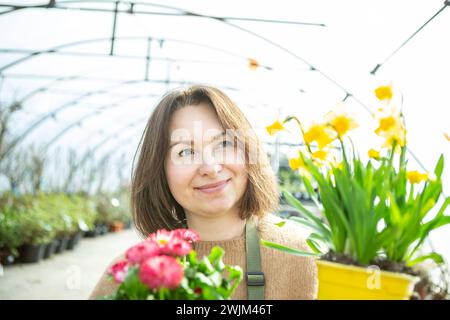 Gärtner mit Blumen Eine reife Frau als Gärtnerin in einer Gärtnerei mit Blumentöpfen. Stockfoto