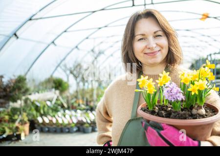 Gärtner mit Blumen Eine reife Frau als Gärtnerin in einer Gärtnerei mit Blumentöpfen. Stockfoto