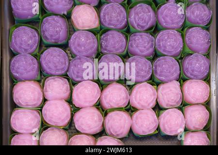 Desserts aus gedämpften Schichten, die in Blumenformen zubereitet werden, in Bananenblattbechern in verschiedenen rosa und lila Farben präsentiert werden Stockfoto