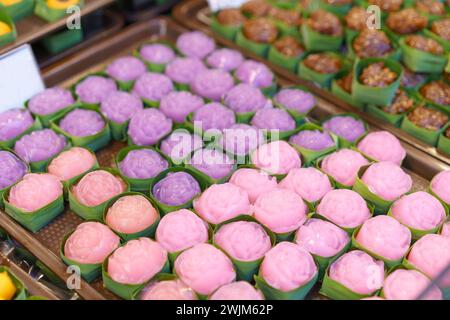 Desserts aus gedämpften Schichten, die in Blumenformen zubereitet werden, in Bananenblattbechern in verschiedenen rosa und lila Farben präsentiert werden Stockfoto