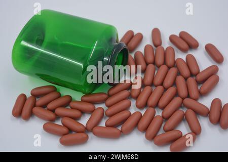 Medizin, Pillen, Medikamente, grüne Flasche mit teuren Vitaminen gefüllt mit braunen Kapseln, flüssigen Tabletten und weißem Plastikdeckel auf weiß. Stockfoto