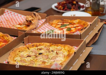 Mehrere Pizzen in Pappschachteln liegen auf einem Tisch ab und bieten eine Vielzahl von käsigen Belägen und herzhaften Zutaten. Ein Grundnahrungsmittel in der Küche, diese Di Stockfoto