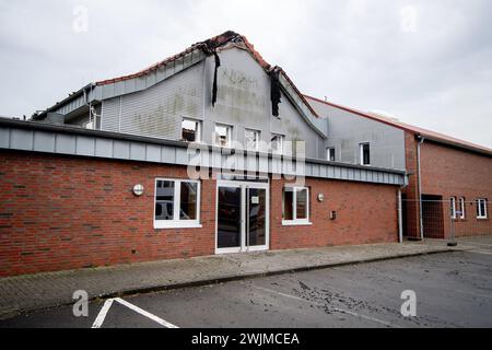 Neermoor, Deutschland. Februar 2024. Baumaterialien hängen vom Dach der abgebrannten Grundschulhalle in Neermoor. Ein Brand zerstörte gestern Abend das Gymnasium in der Neermoor-Grundschule. Starke Winde und leicht brennbare Baumaterialien in der Halle führten dazu, dass sich das Feuer in eine größere Flamme mit fliegenden Funken und starkem Rauch ausbreitete. Quelle: Hauke-Christian Dittrich/dpa/Alamy Live News Stockfoto