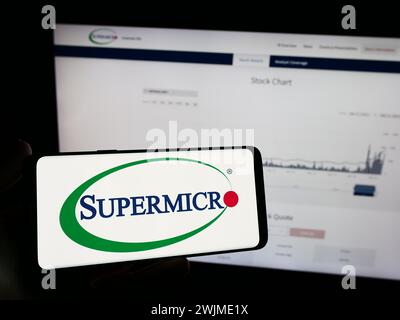Person, die ein Mobiltelefon mit dem Logo des amerikanischen Unternehmens Super Micro Computer Inc. Hält (Supermicro) vor der Webseite. Schwerpunkt auf dem Display des Telefons. Stockfoto