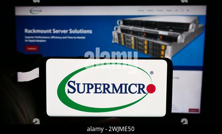 Person, die ein Mobiltelefon mit dem Logo des US-amerikanischen Unternehmens Super Micro Computer Inc. Hält (Supermicro) vor der Business-Webseite. Schwerpunkt auf dem Display des Telefons. Stockfoto