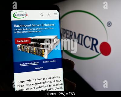Person mit Mobiltelefon auf der Webseite des US-amerikanischen Unternehmens Super Micro Computer Inc (Supermicro) vor dem Logo. Konzentrieren Sie sich auf die Mitte des Telefondisplays. Stockfoto