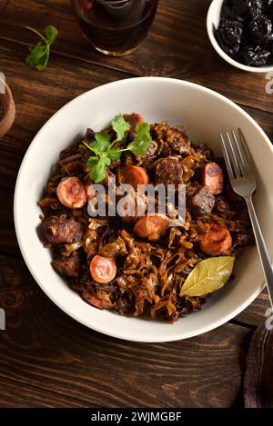 Gedünsteter Kohl (polnische Bigos) mit Sauerkraut, Pilzen, geräuchertem Fleisch und Gewürzen in einer Schüssel auf hölzernem Hintergrund. Nahansicht Stockfoto