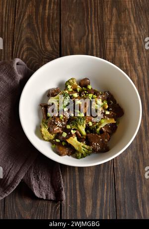 Rindfleisch mit Brokkoli in der Schüssel auf hölzernem Hintergrund. In dünne Scheiben geschnittenes Rindfleisch mit geröstetem Brokkoli. Nahansicht Stockfoto