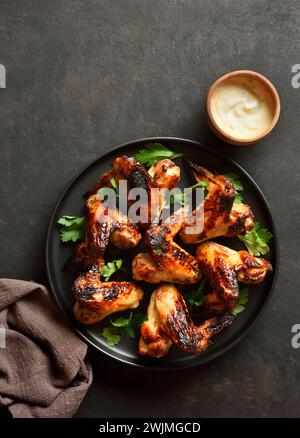 BBQ Chicken Wings serviert mit Sauce auf dunklem Steinhintergrund. Leckeres gegrilltes Hähnchenfleisch zum Abendessen. Draufsicht, flach Stockfoto