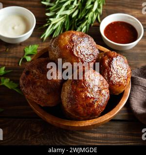 Leckere hausgemachte Schnitzel aus Hackfleisch in einer Schüssel serviert mit Sauce auf Holztisch. Nahansicht Stockfoto