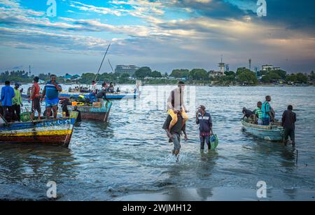 Ein Portier trägt einen Fischer auf seinen Schultern von traditionellen hölzernen Dhow-Booten, die mit Fischern überfüllt sind, nachdem sie am Abend in Kivukoni F ankommen Stockfoto