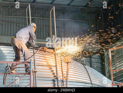 Arbeiter verwenden einen Gasbrenner, der die Metallblechwand des Wassertanks im Werk schneidet. Stockfoto