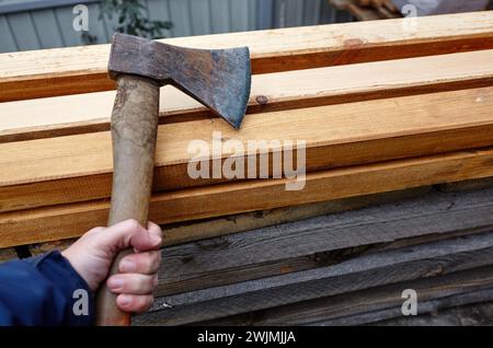 Mann mit Axt. Axt in der Hand. Ein starker Mann hält eine Axt in den Händen vor dem Hintergrund von Feuerholz. Selektiver Fokus, unscharfer Hintergrund Stockfoto