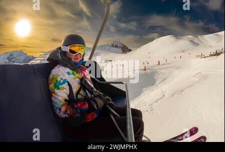 Junge Frau im Sessellift bei Sonnenuntergang, in einem Skigebiet rund um den Berg Sela, Selaronda, Dolomiten, Italien Stockfoto
