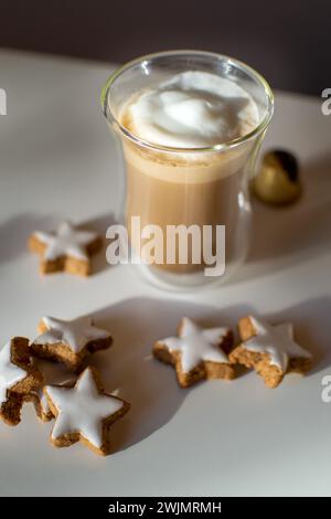Kaffee mit weißem Milchschaum auf einem weißen Tisch unter Sternkeksen Stockfoto