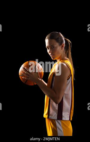 Selbstbewusste Basketballspielerin, bereit für das Spiel, posiert in dunkler Umgebung. Stockfoto