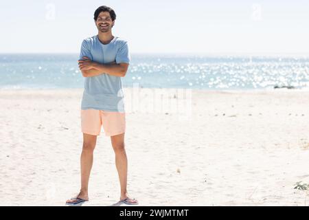 Junger birassischer Mann steht selbstbewusst an einem sonnigen Strand mit Kopierraum Stockfoto