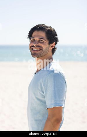 Ein junger, birassischer Mann lächelt hell am Strand Stockfoto